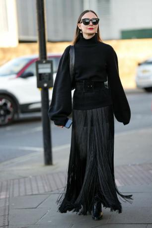 Žena v černém želvím krku s dlouhým rukávem a dlouhou černou třásňovou sukni