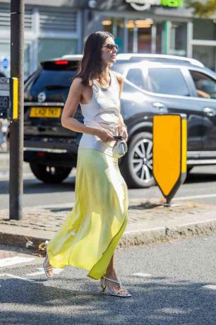 Mujer viste camiseta sin mangas blanca, falda verde amarilla y tacones plateados.