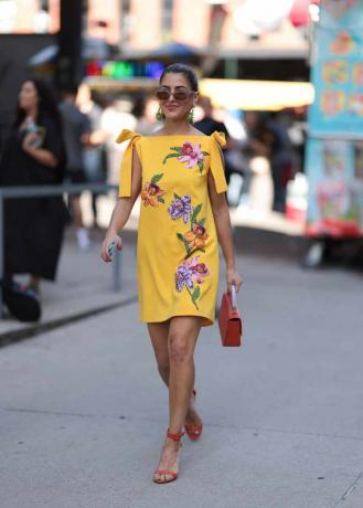 La mujer lleva un vestido floral amarillo con accesorios rojos.