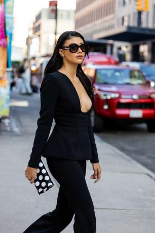 Vrouw met laag uitgesneden peplumtop en zwarte broek en zwart-witte tas