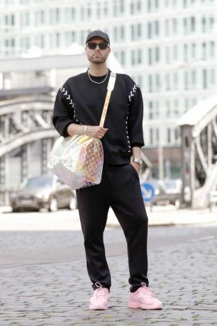 Muž nosí černou teplákovou soupravu s růžovými teniskami a průhlednou taškou, což je nápad na pýchu.