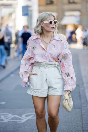 Femme portant un short blanc avec un bouton rose à motifs et un sac jaune et des lunettes de soleil blanches.