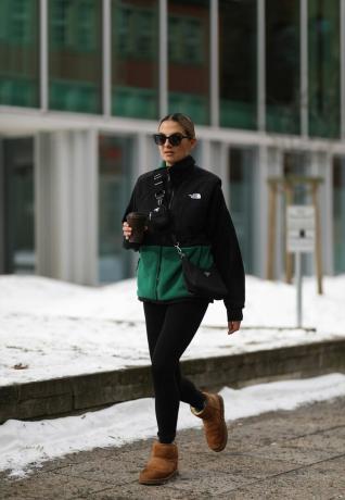 Une femme portant des leggings noirs, des bottes UGG marron et une polaire North Face noire et verte avec un sac bandoulière Prada