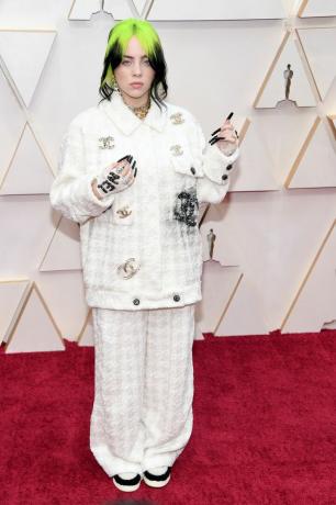 Billie Eilish in einem weißen Chanel-Anzug, Spitzenhandschuhen und neongrünen und schwarzen Haaren