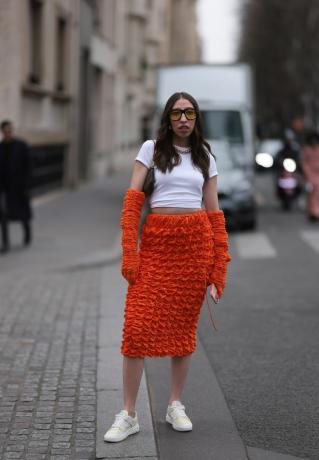 Žena má na sobě bílé tričko a oranžovou texturovanou midi sukni