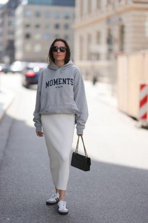 Femme portant un sweat à capuche gris et une jupe longue blanche.