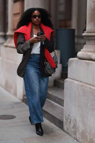 La femme porte un pull rouge, un blazer foncé et un jean large avec un sac Dior