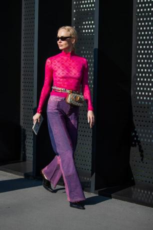 ترتدي المرأة بنطال جينز باللون البنفسجي والوردي مع بلوزة منقوشة شفافة.