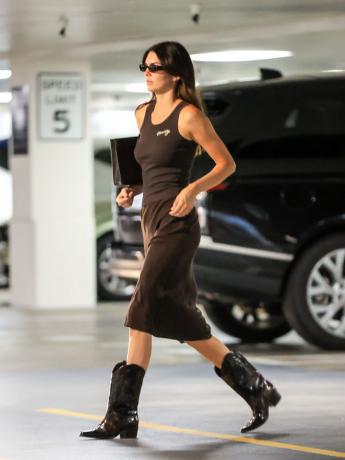 Mengenakan sepatu bot koboi berwarna coklat, Kendall Jenner menunjukkan cara menata sepatu bot koboi dengan rok midi dan tank top, ide outfit sepatu bot koboi untuk tahun 2023.