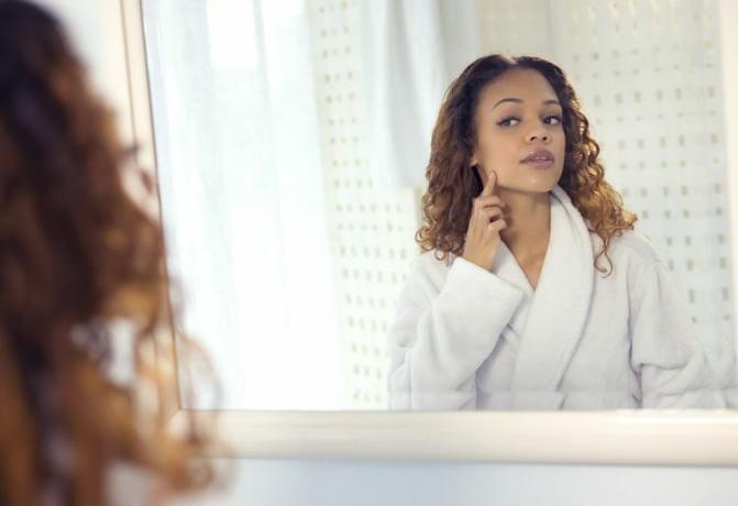 Une femme qui regarde sa peau dans le miroir.