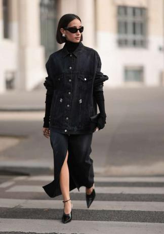 ženska, oblečena v črno preveliko jeans jakno, črno želvo in črno midi krilo