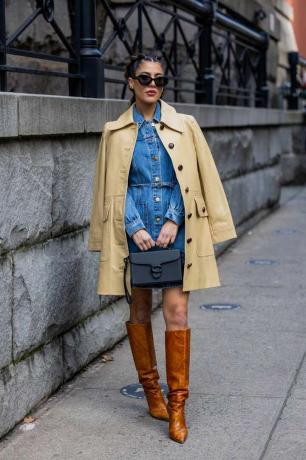 Žena nosí béžový trenčkot přes džínové šaty během týdne módy v New Yorku