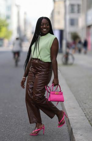 Loui Opoku indossa una t-shirt verde, pantaloni di pelle marroni e sandali rosa, un outfit con pantaloni di pelle da provare per il 2023