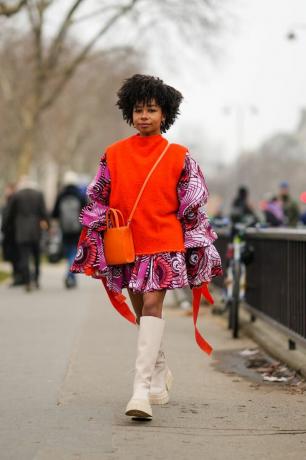 Жена носи наранџасти џемпер прслук и штампану хаљину