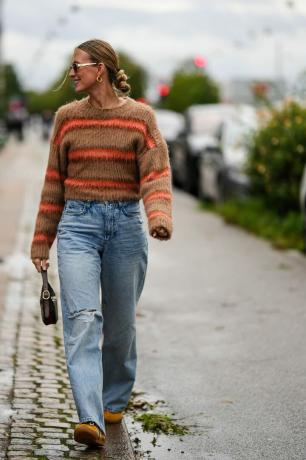 Женщина носит полосатый свитер и джинсы.