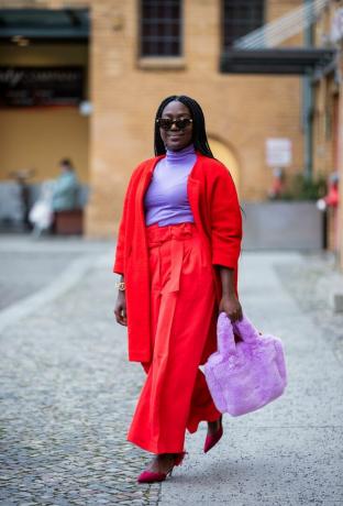 Lois Opoku indossa un cardigan rosso, pantaloni rossi e un top a collo alto viola chiaro, un'idea outfit dolcevita 2023 per le donne. 