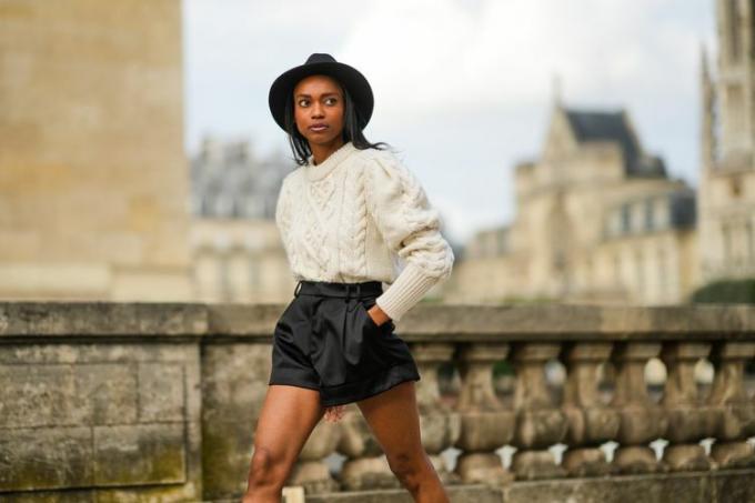 Femme portant un chandail blanc avec un short noir et un chapeau noir.