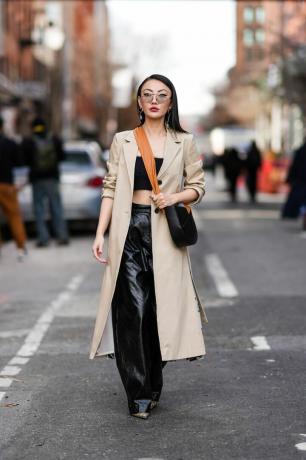 Nainen käyttää beigeä trenssitakkia nahkahousujen päällä New Yorkin muotiviikolla
