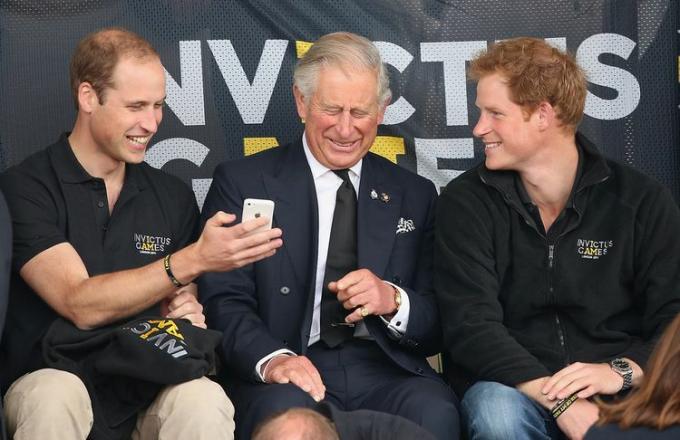 Le prince Harry, le prince William et le roi Charles rient de quelque chose sur un téléphone aux Jeux Invictus 2014