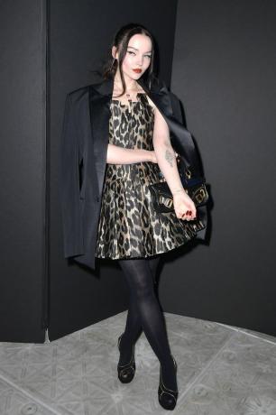 Dove Cameron na sobě šaty se zvířecím potiskem a černý kabát.