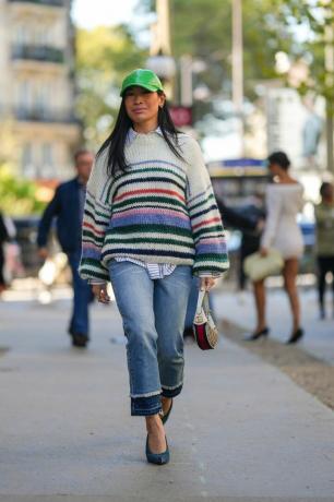 Mujer con un suéter a rayas con jeans y una gorra de béisbol verde. 