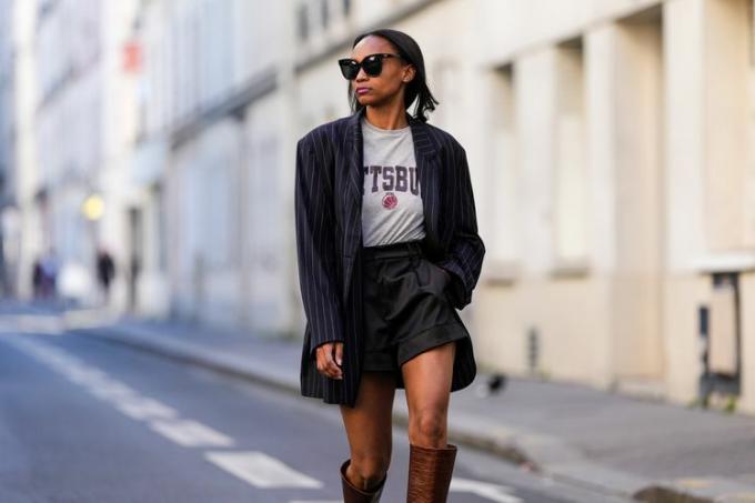 Femme portant un short noir avec un tee-shirt gris et un blazer à rayures et des bottes marron hautes. 