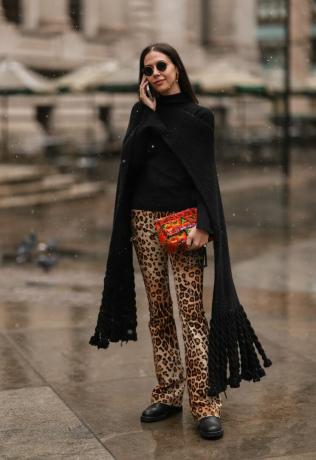 La femme porte du marron et du noir avec un pantalon imprimé léopard et une écharpe noire.