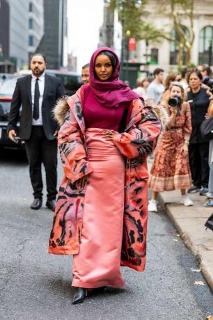 Halima Aden portant un foulard, une jupe en soie couleur saumon, un manteau imprimé + une tenue d'invité de mariage
