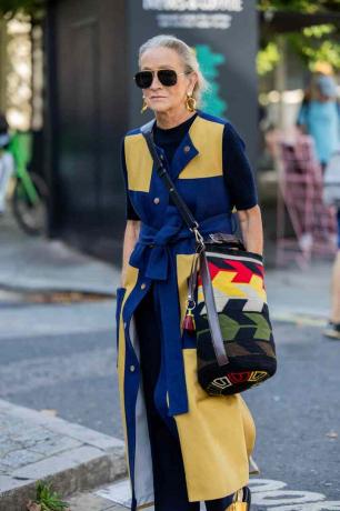 Een vrouw met een gele en blauwe jurk en een veelkleurige tas