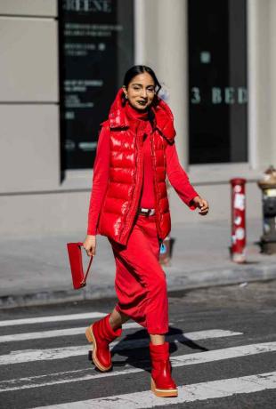 Een vrouw draagt ​​een rood puffervest, jurk, laarzen en witte riem in NYC